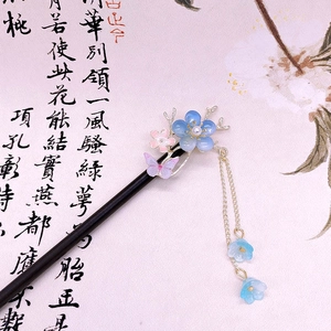 Detail of wooden hair stick with blue butterfly, pink floral petals and metallic tassels