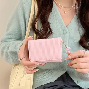 Pink trifold wallet with pleated texture and bow charm pendant held by hand