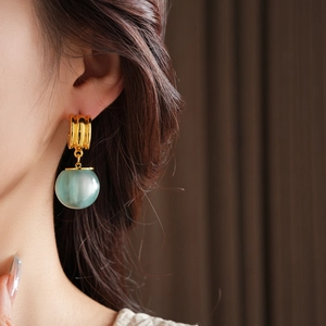 Close-up of model wearing gold irregular resin pendant earrings with green bead