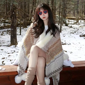 Close-up of ethnic style knit poncho with faux fur collar and pom-poms in snowy forest