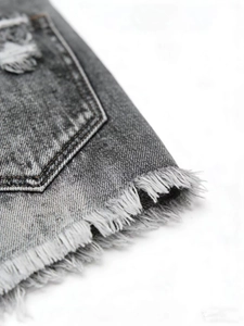 Detailed close-up of frayed raw hem and denim texture on grey distressed denim shorts
