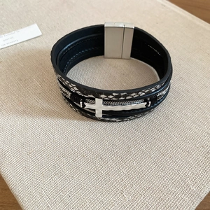 Détail d'un bracelet en cuir tressé avec croix en argent et fermoir magnétique