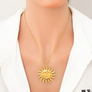 Close-up of a gold sun face pendant necklace worn by a model on a white top