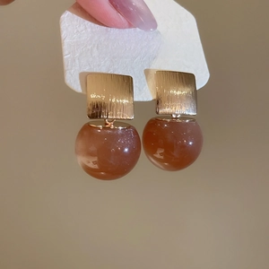 Detailed shot of golden square studs with translucent brown resin ball pendants