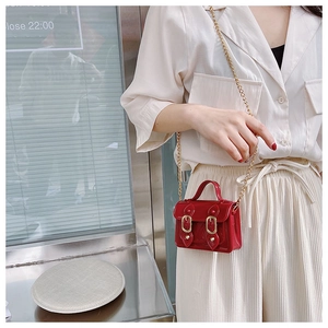 Close-up of bright red patent leather satchel featuring gold double-buckles and metal chain