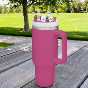 Detailed view of a pink insulated 40oz tumbler with a cute cat charm and straw outdoors