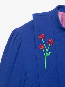 Detail of royal blue hooded jacket featuring red and green floral embroidery with striped lining