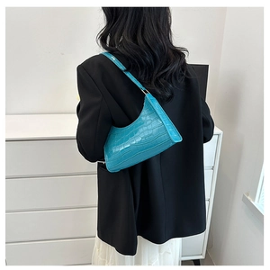 Detail of lake blue crocodile pattern underarm bag worn with a stylish black blazer