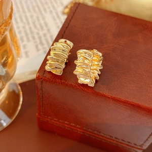 Macro detail of irregular gold hoop earrings with pleated texture on leather box