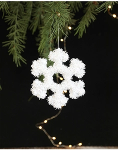 Detailed view of white snowflake Christmas ornament hanging on a green pine branch