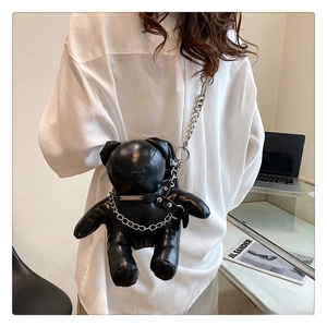 Detail of a black PU leather bear crossbody bag with silver chains on white shirt