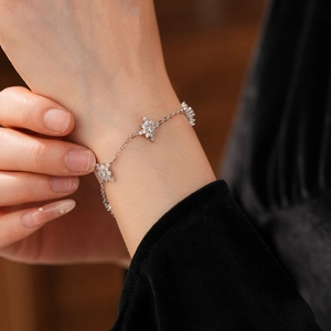Détail d'un bracelet en argent avec étoiles en zircon porté au poignet et breloques neige