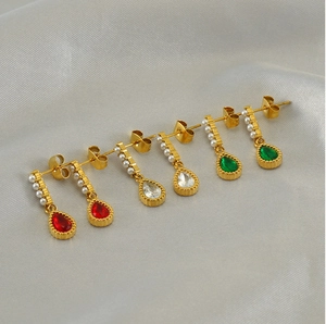 Detailed view of gold earrings with red white and green teardrop stones on silk fabric