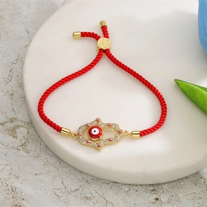 Red braided evil eye hamsa hand bracelet with gold finish and zircon stones on white marble