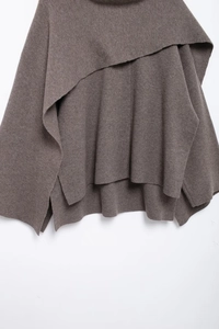 Detail view of the brown knitted asymmetric poncho wrap with a soft layered texture