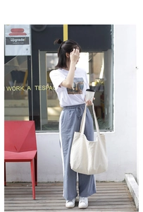 Casual cream-colored canvas tote bag shown being held by a model in a street setting