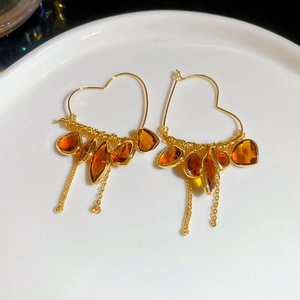 Detailed close-up of 18K gold plated heart earrings with crystal tassels on a white plate