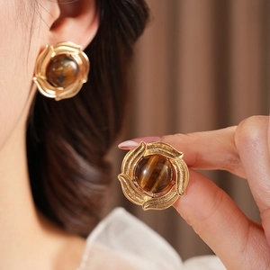Detailed close-up of vintage gold earrings featuring tiger eye stones and feather texture