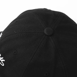 Close-up of black cotton twill baseball cap crown with button and white embroidery detail