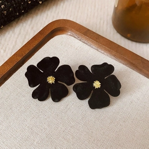 Detail of black flower earrings with gold centers on a rustic wooden tray and fabric