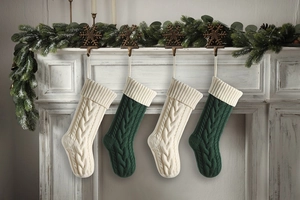 Detail of four knitted Christmas stockings with cable patterns hanging on a decorated fireplace