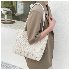 Close-up of beige straw tote bag featuring green leaf embroidery and cotton rope straps