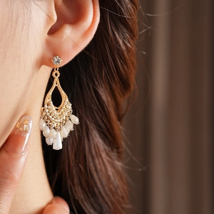 Detail of bohemian gold drop earrings with white bead tassels and rhinestone accents
