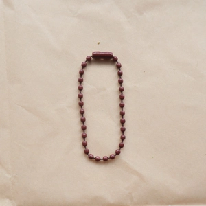 Detailed top view of a 2.4mm brown metal bead chain connector on crinkled paper