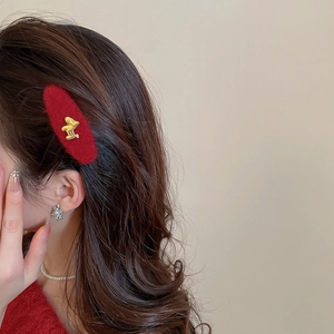 Detailed view of red velvet hair clip with gold metal emblem on wavy brunette hair