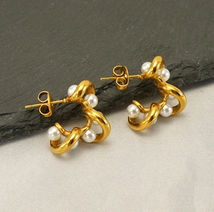 Close-up of golden twist knot earrings with embedded white pearls on stone background