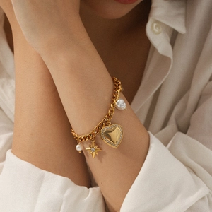Detail eines goldenen Panzerkettenarmbands mit Diamant-Herz, Sternanhänger und Perlen