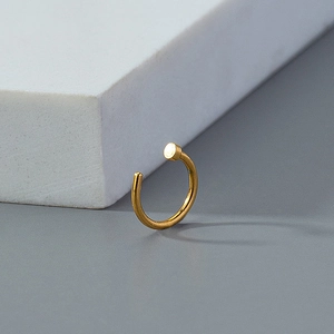 Detail of a golden non-piercing nose ring clip with flat disk end on a textured surface