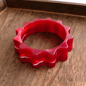 Détail du bracelet en acrylique rouge ondulé sur un fond de texture en bois vintage