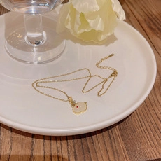 Golden titanium steel necklace with white circular pendant on elegant white ceramic plate
