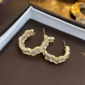 Close-up of golden C-shaped hoop earrings with inlaid clear gems in a jewelry box