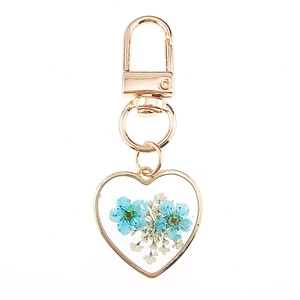Macro shot of heart-shaped resin keychain with blue dried flowers and golden lobster clasp