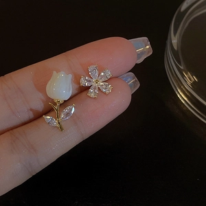 Macro view of gold tulip and floral stud earrings with white petals and clear zircon stones