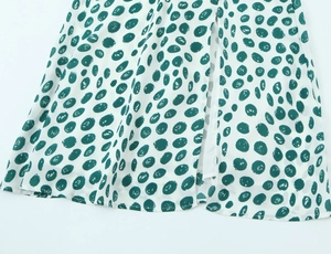 Detailed close-up showing side slit and green polka dot pattern on white summer dress fabric