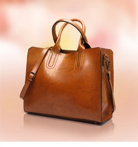 Brown leather handbag with dual top handles and a detachable shoulder strap on reflective base