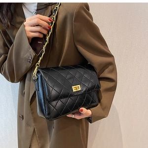 Detail of black quilted leather shoulder bag with gold chain strap and metal swivel lock
