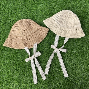 Flat lay of khaki and cream crochet straw hats with lace ties on green grass background