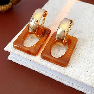 Close-up of geometric C-shaped gold hoop earrings with amber resin pendants on a book