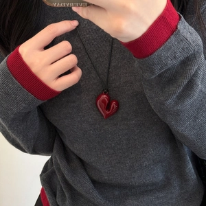 Collana con cuore rosso minimalista e cordino nero regolabile su maglione grigio