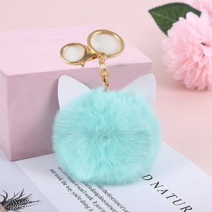 Close-up of mint green fluffy cat ear keychain with golden ring on a pink background
