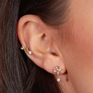 Close-up of golden cartilage studs with flower and heart butterfly chain tassel details