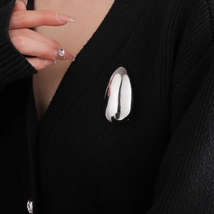 Macro view of a silver teardrop brooch on a black knit fabric background