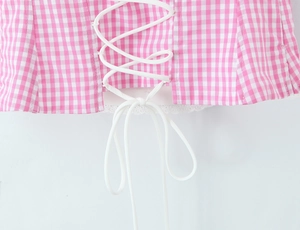 Detail of pink plaid top featuring white lace trim and adjustable lace-up ribbon closure