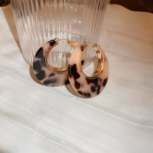 Close-up of leopard print resin earrings with gold plating next to textured glass
