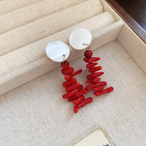 Detail of red coral resin tassels and white shell stud earrings on beige jewelry box