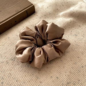 Gros plan sur le chouchou en soie marron aux plis naturels sur tissu en maille beige
